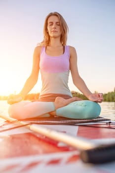 Young beautiful woman meditating in a sea at SUP paddleboarding. Healthy lifestyle. Girl in yoga pose relaxing in calm water.