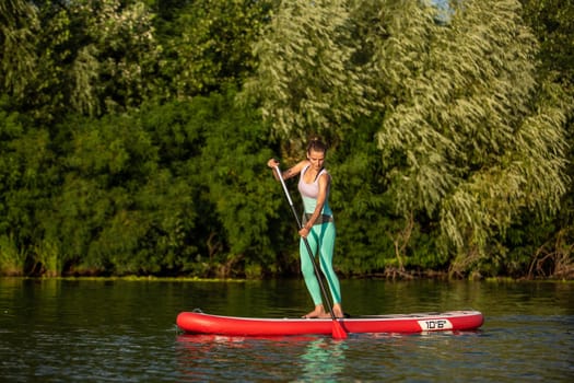 Young athletic woman doing fitness on a board with an oar on a lake. The concept of a healthy lifestyle. Sport. Yoga. Hobby