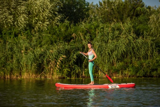 Young athletic woman doing fitness on a board with an oar on a lake. The concept of a healthy lifestyle. Sport. Yoga. Hobby
