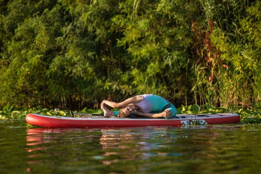 Young woman are doing yoga on a stand up paddle board SUP on a beautiful lake or river. The concept of a healthy lifestyle. Sport. Yoga. Hobby