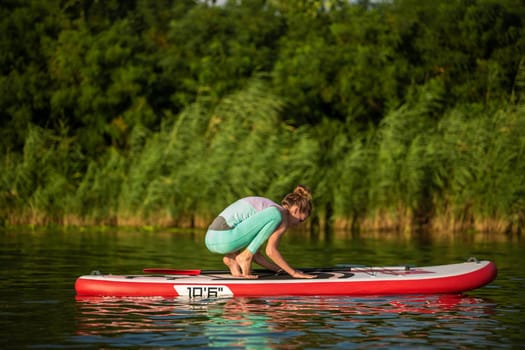 Young woman are doing yoga on a stand up paddle board SUP on a beautiful lake or river. The concept of a healthy lifestyle. Sport. Yoga. Hobby