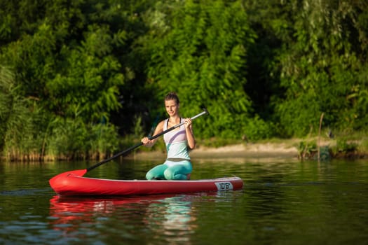 Young athletic woman doing fitness on a board with an oar on a lake. The concept of a healthy lifestyle. Sport. Yoga. Hobby