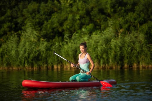 Young athletic woman doing fitness on a board with an oar on a lake. The concept of a healthy lifestyle. Sport. Yoga. Hobby