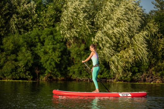 Young athletic woman doing fitness on a board with an oar on a lake. The concept of a healthy lifestyle. Sport. Yoga. Hobby