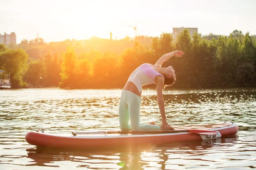 Young woman doing yoga on sup board with paddle. Yoga pose, side view - concept of harmony with the nature, free and healthy living, freelance, remote business.