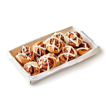 Soft and fluffy cinnamon swirls topped with sugar glaze in paper box isolated on white background. Popular baked sweets