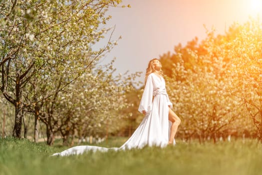 Blond blooming garden. A woman in a white dress walks through a blossoming cherry orchard. Long dress flies to the sides