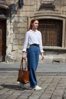 photo of a woman with a leather bag. the girl is dressed in jeans, a white blouse and sneakers