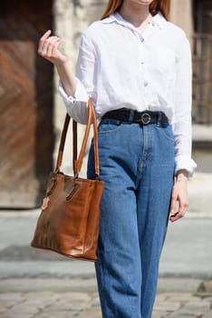 photo of a woman with a leather bag. the girl is dressed in jeans and a white blouse