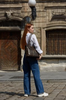 photo of a woman with a leather bag. the girl is dressed in jeans, a white blouse and sneakers