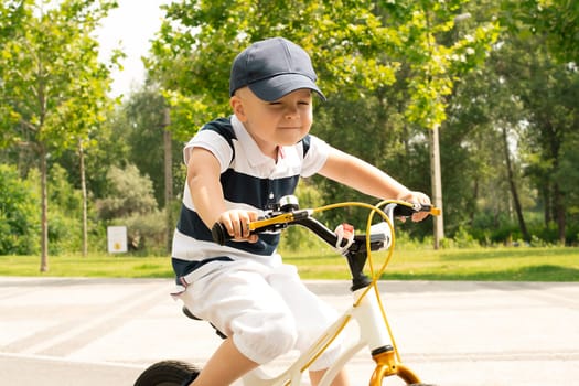 Sport concept. Boy on a bicycle close-up. A small beautiful, happy, Caucasian boy 4 years old in a cap and a striped T-shirt rides a bicycle along the bike path in the summer outdoors.