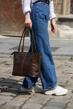 photo of a woman with a leather bag. the girl is dressed in jeans, a white blouse and sneakers