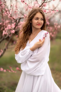 Woman peach blossom. Happy curly woman in white dress walking in the garden of blossoming peach trees in spring.