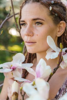 Magnolia flowers. Happy woman enjoys by blooming magnolia tree and sniffs it flowers with closed eyes in spring garden. Portrait