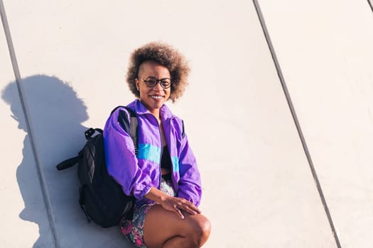 portrait of a smiling african american young woman in sports clothes leaning on an urban wall, concept of active lifestyle and urban sport, copy space for text