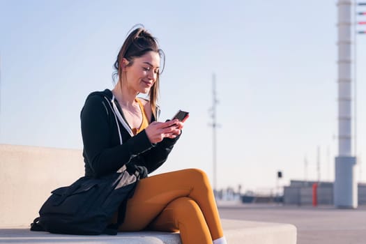 sportive woman sitting outdoors in the city using a mobile phone, concept of technology of communication and urban lifestyle, copy space for text