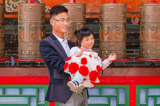 A dad and a young girl pose in front of aniken prayer wheels of a temple in Kumbum Jampaling monastery complex, Xining, China