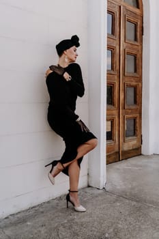 Stylish woman in the city. Fashion photo of a beautiful model in an elegant black dress posing against the backdrop of a building on a city street.