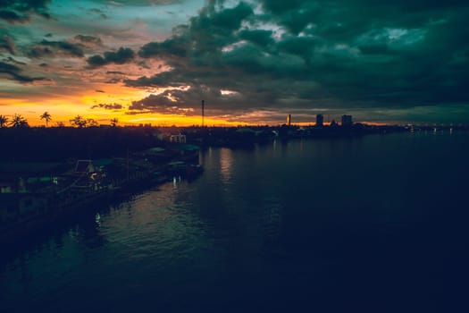 Panorama Cityscape at sunset with large river at foreground and strom clouds at background in Thailand.