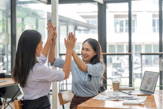 Excited asian business team giving high five at office meeting motivated by victory, achievement or good work result.