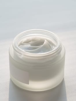 Glass jar of luxury face cream. Open jar with beautidul swirls of white cream in natural daylight. Mockup for cosmetic cream jar product.