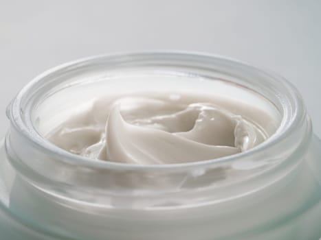 Glass jar of luxury face cream. Close up open jar with beautiful swirls of white cream in natural daylight. Texture of cosmetic cream in jar