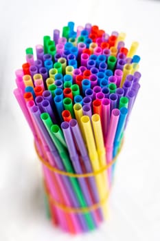 a lot of bright multicolored cocktail tubes are clamped with an elastic band in a bundle on a white background. Multicolored Plastic Cocktail Tubes