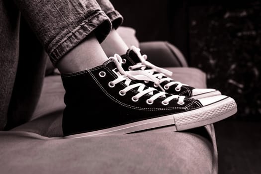 the girl's legs are shod in classic sneakers. black and white photo. Sneakers on the girl's foot. Feet of a teenager in casual new sneakers on the couch close-up.