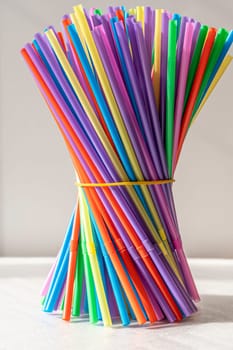 a lot of bright multicolored cocktail tubes are clamped with an elastic band in a bundle on a white background. Multicolored Plastic Cocktail Tubes