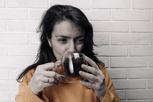 a pretty Caucasian middle-aged woman after stress restores her mental balance with a mug of healing tea. glass transparent mug with delicious fragrant tea. Enjoying the moment, mental health. Emotional burnout