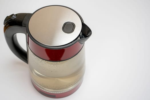 glass electric kettle with beautiful red walls filled with water for making tea on a white background side view from above.