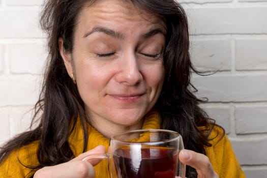 a pretty Caucasian middle-aged woman drinks tea and closes her eyes with pleasure. transparent mug with delicious fragrant tea. Enjoying the moment, mental health and positive emotions