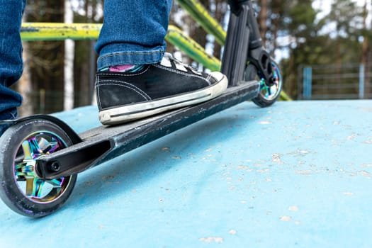 Rider boy legs close up in sneakers on stunt scooter on the skate park ramp. A boy on a scooter in a skate park performs jumps and tricks. extreme city sports outdoor Extreme jumping on a scooter. The concept of a healthy lifestyle. sports leisure