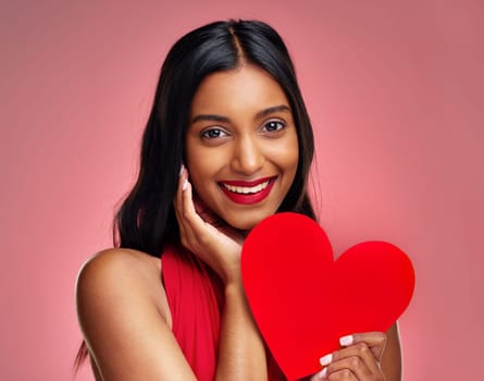 Portrait, heart and romance with a woman on a pink background in studio for love or affection. Smile, emoji and social media with a happy young female holding a shape or symbol on valentines day.