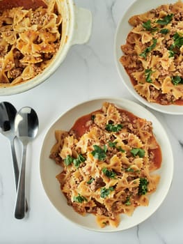Pasta Farfalle with tomato sauce and ground meat in plate on white marble tabletop. Idea and recipes for easy, simple lunch or dinner one-pot meat goulash. Top down view or flat lay. Vertical
