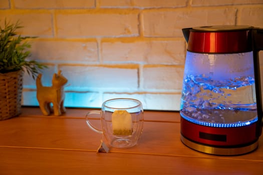 A glass electric kettle on a wooden table and a transparent mug with a bag of delicious tea. High quality photo