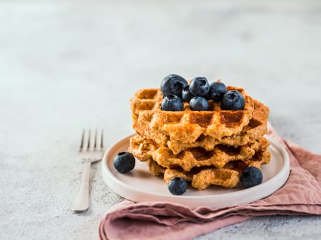 Easy healthy gluten free oat waffles with copy space. Stack of appetizing homemade waffles with oat flour decorated blueberries, on plate over light gray cement background