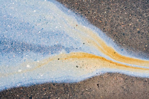 Spots of oil or gasoline are scattered randomly on the asphalt after rain. Abstract background close-up