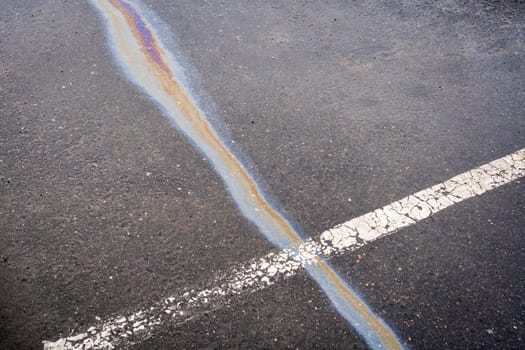 After rain on wet pavement, an iridescent spill of oil or gasoline crosses the dividing line.