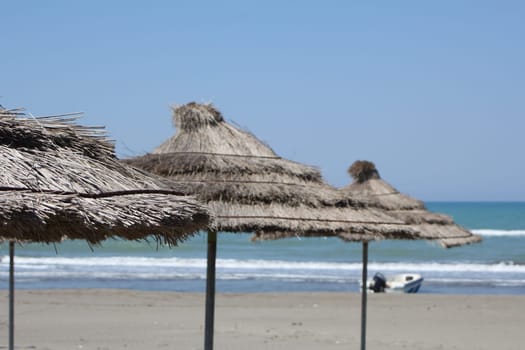 Mediterranean sand beach and summer sea blue water. Three straw umbrellas