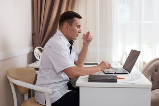 male doctor in white medical uniform using computer laptop in health clinic or hospital. online consultation for domestic health treatment