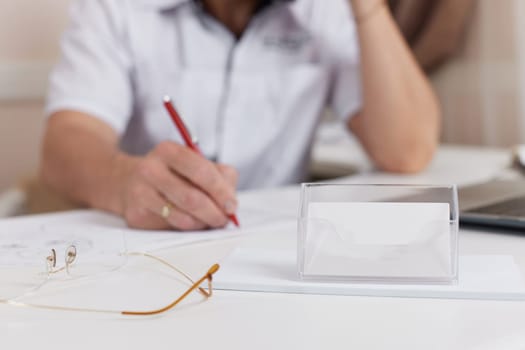 blurred doctor writing and empty business card on table on focus in clinic