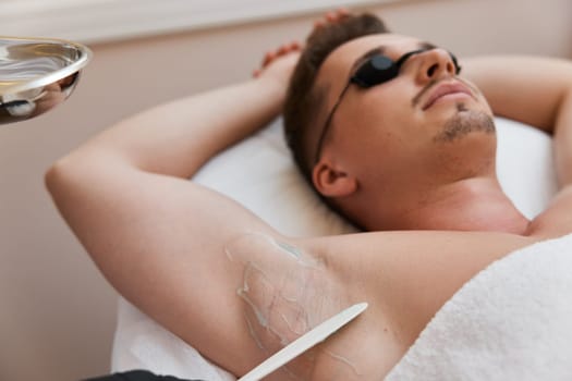 young man with protective goggles undergoes procedure of arm pit laser epilation in clinic