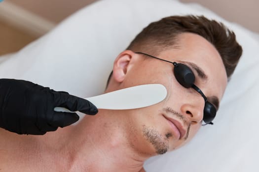 beautician applies cooling gel to male facefor receiving epilation in beauty center.