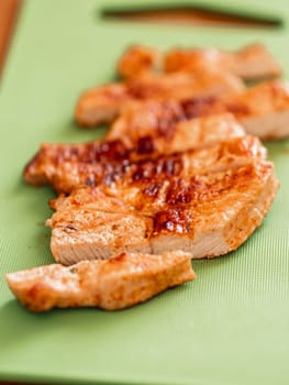 Grilled turkey meat steak sliced on cutting board over wooden tabletop. Perfect ready-to-eat turkey fillet on green cutting board. Striped cooked fillet of turkey meat. Vertical. Copy space