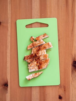Grilled turkey meat steak sliced on cutting board over wooden tabletop. Perfect ready-to-eat turkey fillet on green cutting board top view or flat lay. Striped cooked fillet of turkey meat. Vertical