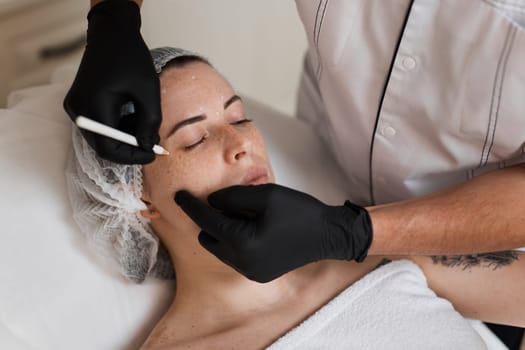 male cosmetologist marking skin of caucasian woman with white pencil. facial marking for aesthetic procedure.