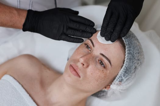 beautician cleanses skin of beautiful woman with cotton sponge. Perfect cleaning, spa treatment skincare face.