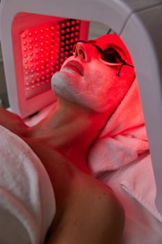 Woman in protective glasses getting facial treatment with led therapy. LED mask at the beauty clinic