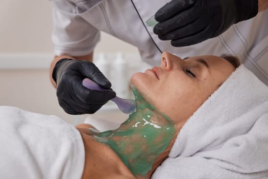 beautician applies green alginate mask to the face of beautiful woman in the spa salon. spa treatments